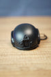 Front view of a black FAST MT helmet bottle opener keychain with tactical mount details, rounded helmet shell, and compact desk display.