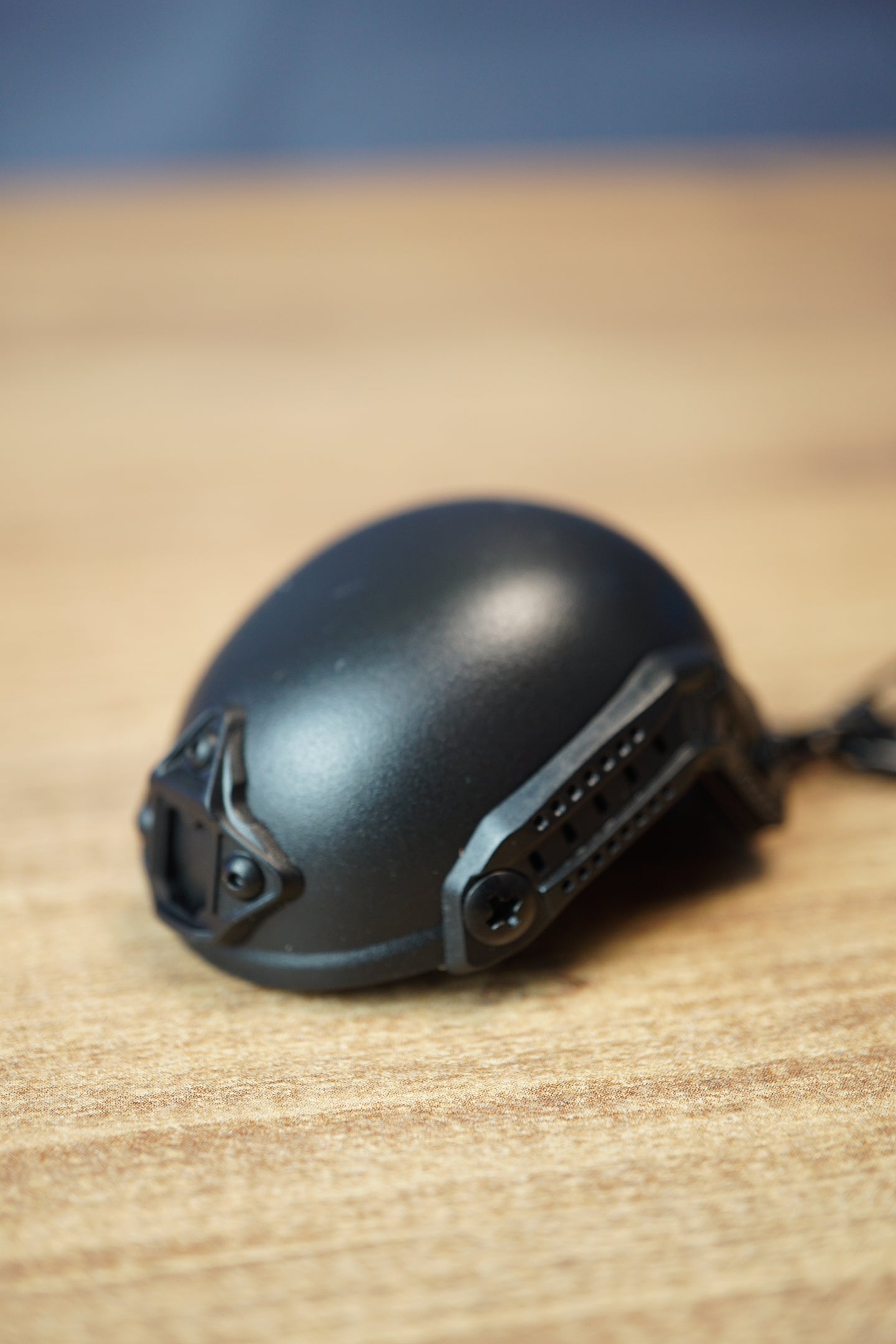 Black FAST MT helmet bottle opener keychain inspired by Tarkov, shown from the side with rail details, front mount, and keyring on a wooden desk.