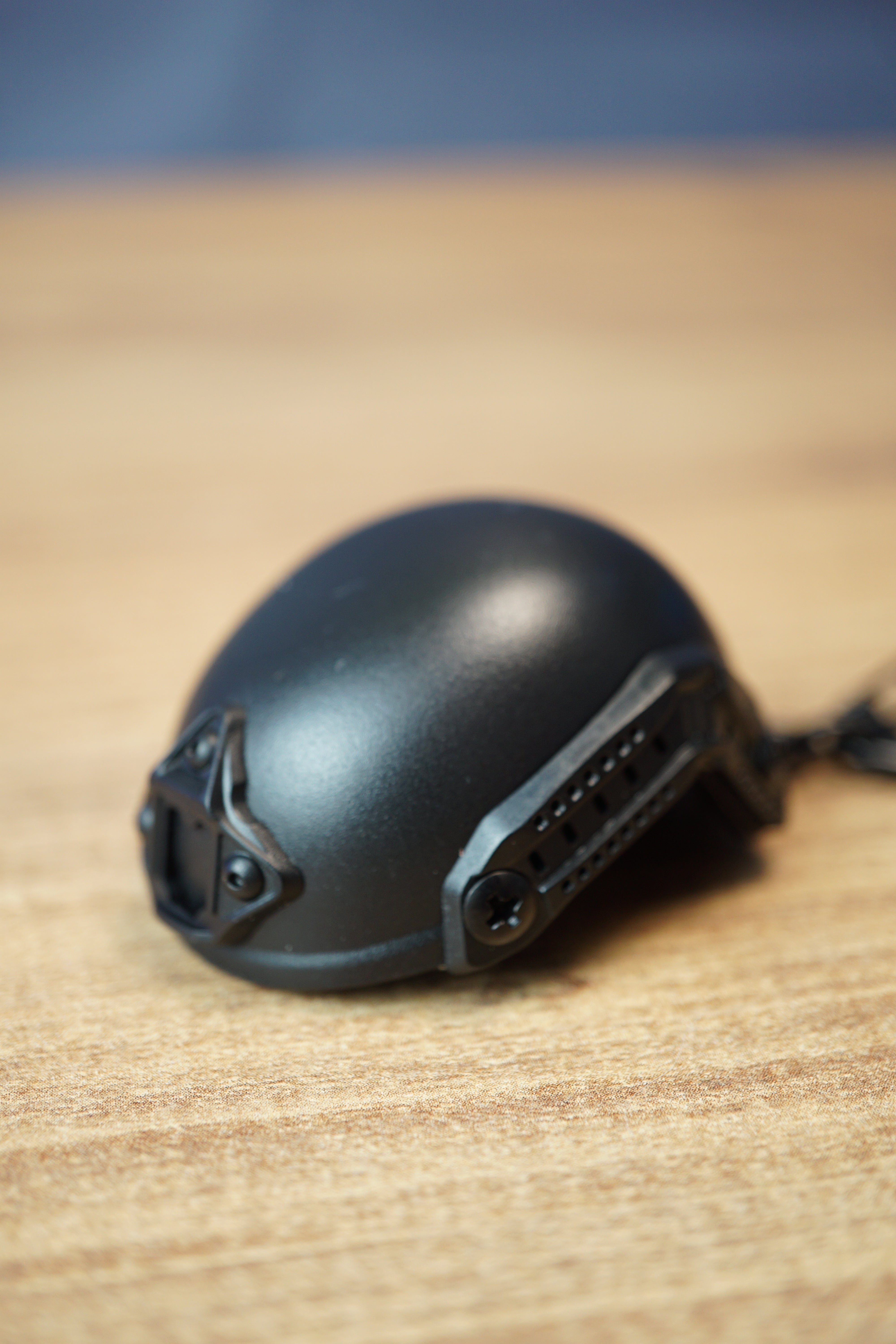 Black FAST MT helmet bottle opener keychain inspired by Tarkov, shown from the side with rail details, front mount, and keyring on a wooden desk.