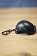 Side view of a FAST MT helmet bottle opener keychain featuring a black helmet shell, rail detail, attached keyring, and wooden tabletop background.
