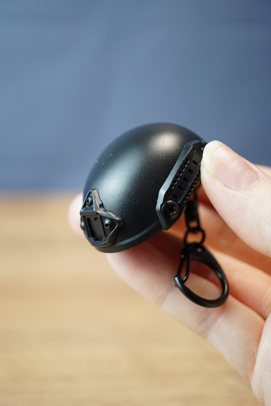 Close-up handheld FAST MT helmet bottle opener keychain showing the black helmet shell, front mount, side rail detail, and compact keychain size.
