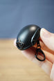 Close-up handheld FAST MT helmet bottle opener keychain showing the black helmet shell, front mount, side rail detail, and compact keychain size.