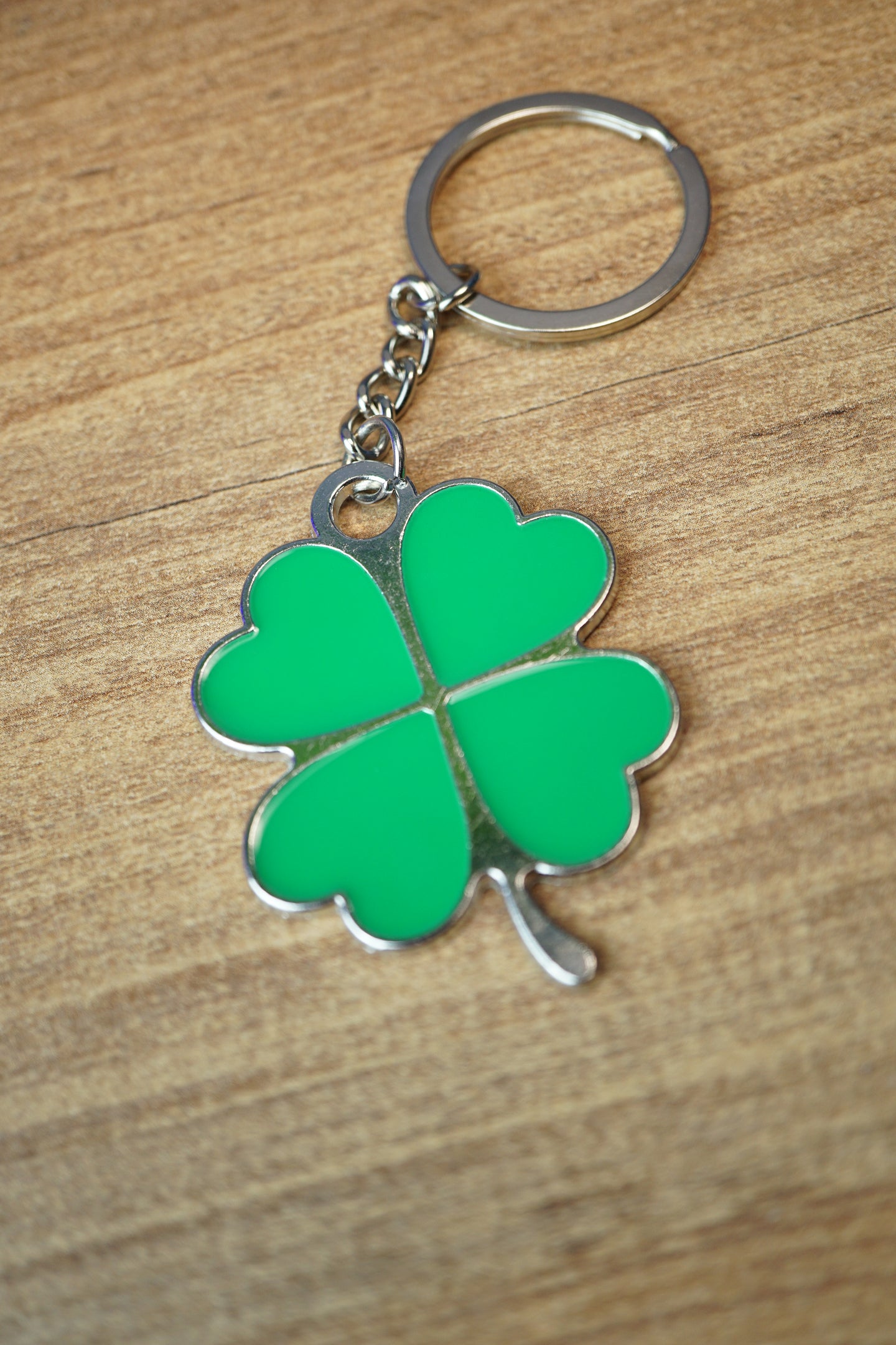 Lucky green four leaf clover keychain with silver outline and attached keyring, photographed from above on a wood grain tabletop.