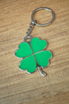 Lucky green four leaf clover keychain with silver outline and attached keyring, photographed from above on a wood grain tabletop.