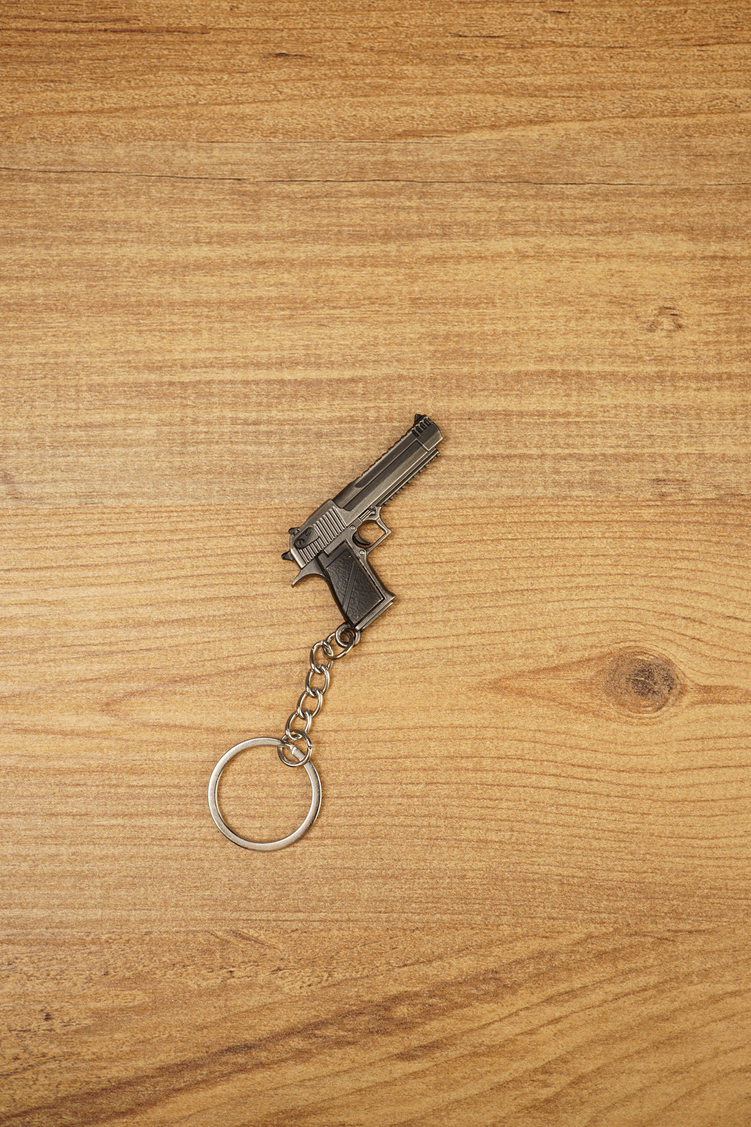 Desert Eagle-style gamer gun keyring on a wood background, angled to show the compact pistol shape, chain link and round keyring loop