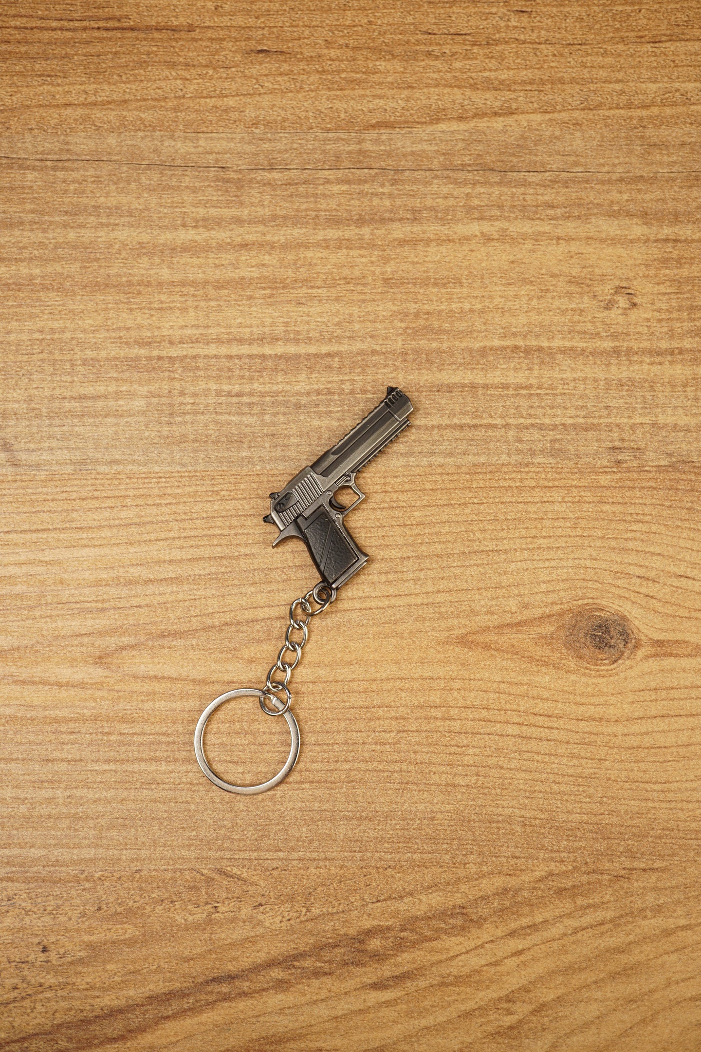 Desert Eagle-style gamer gun keyring on a wood background, angled to show the compact pistol shape, chain link and round keyring loop