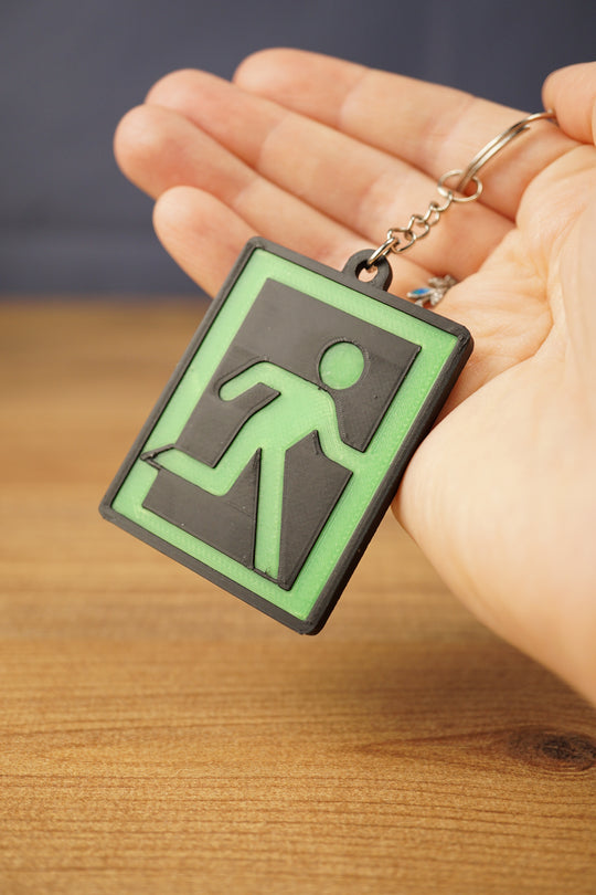 Hand holding a green and black extraction sign keyring, showing the raised 3D printed running figure design and metal keychain.