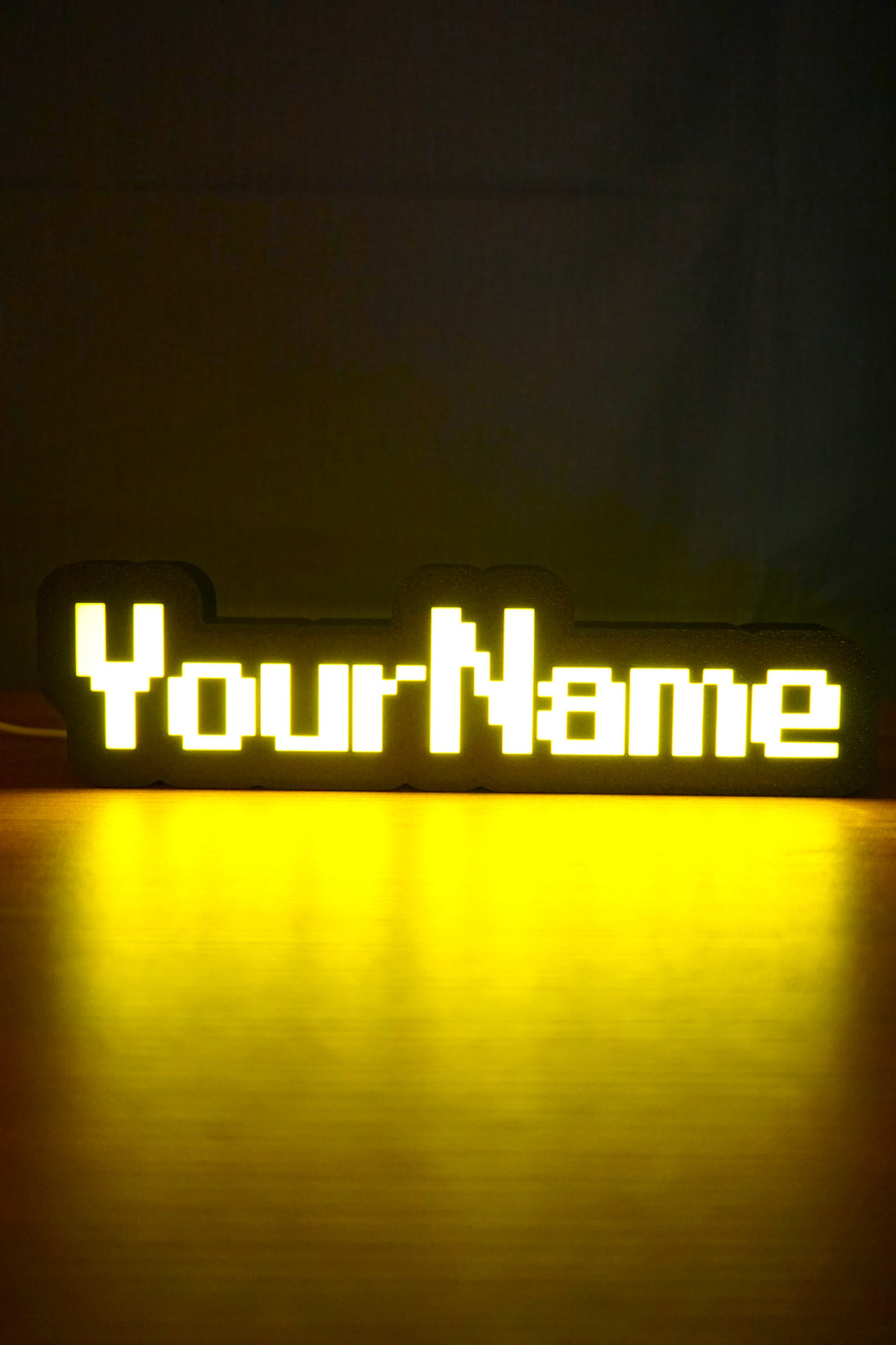 Illuminated YourName LED name sign glowing bright yellow in a dark room with a nostalgic RuneScape-style font design.