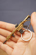 Gold rifle keyring held in hand with key loop attached, showing detailed miniature gaming charm from the side.