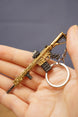 Gold rifle keyring held in hand with key loop attached, showing detailed miniature gaming charm from the side.