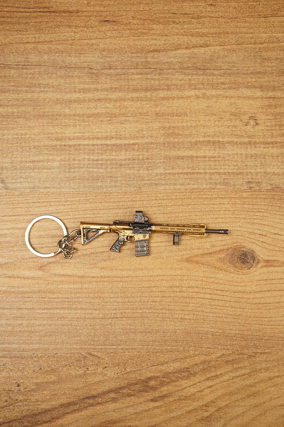 Gold tactical rifle keyring with detailed sight, magazine and barrel shown on wood as a gaming backpack charm.