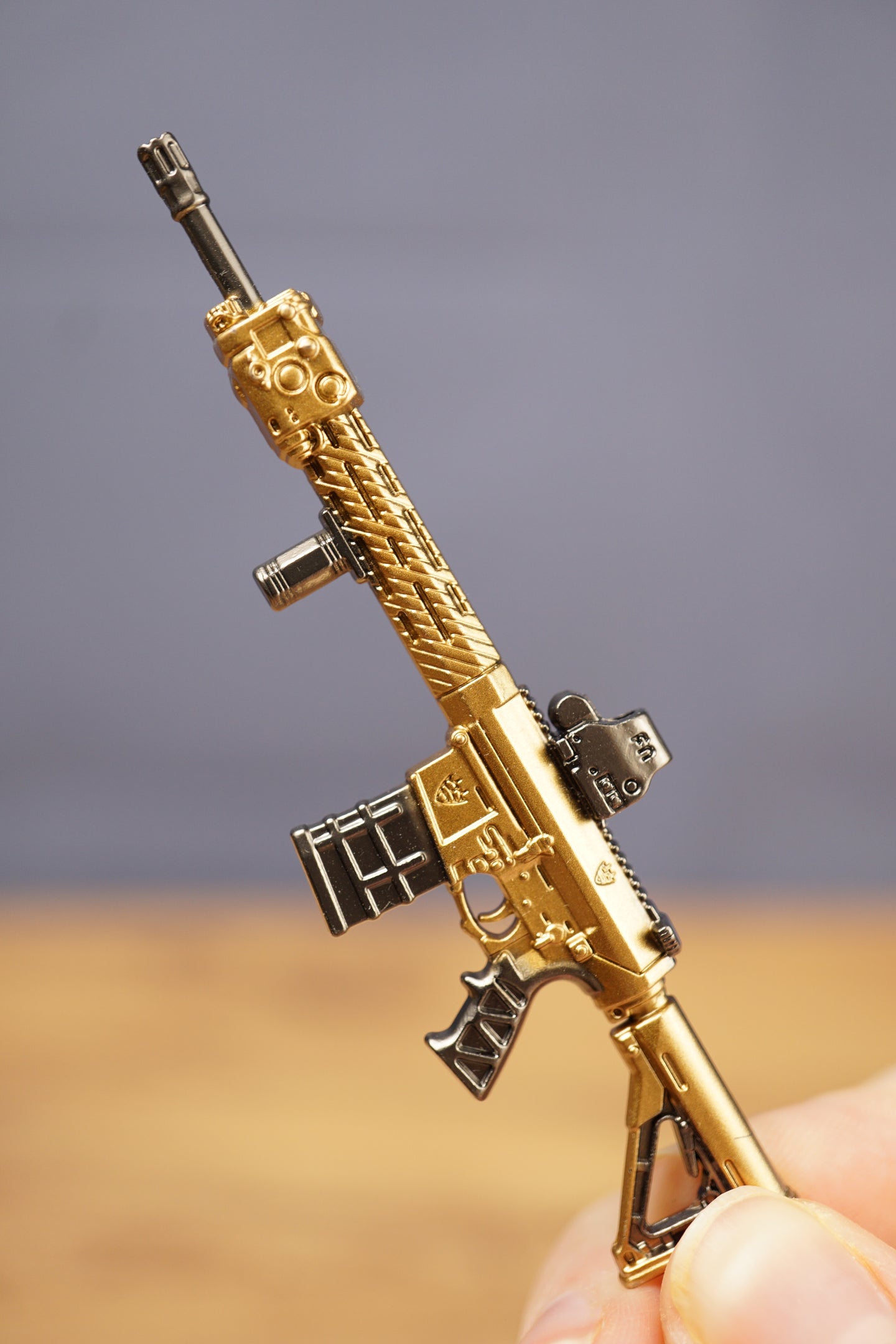 Gold tactical rifle keyring resting in hand with metal key loop, designed as a collectible FPS gamer accessory.