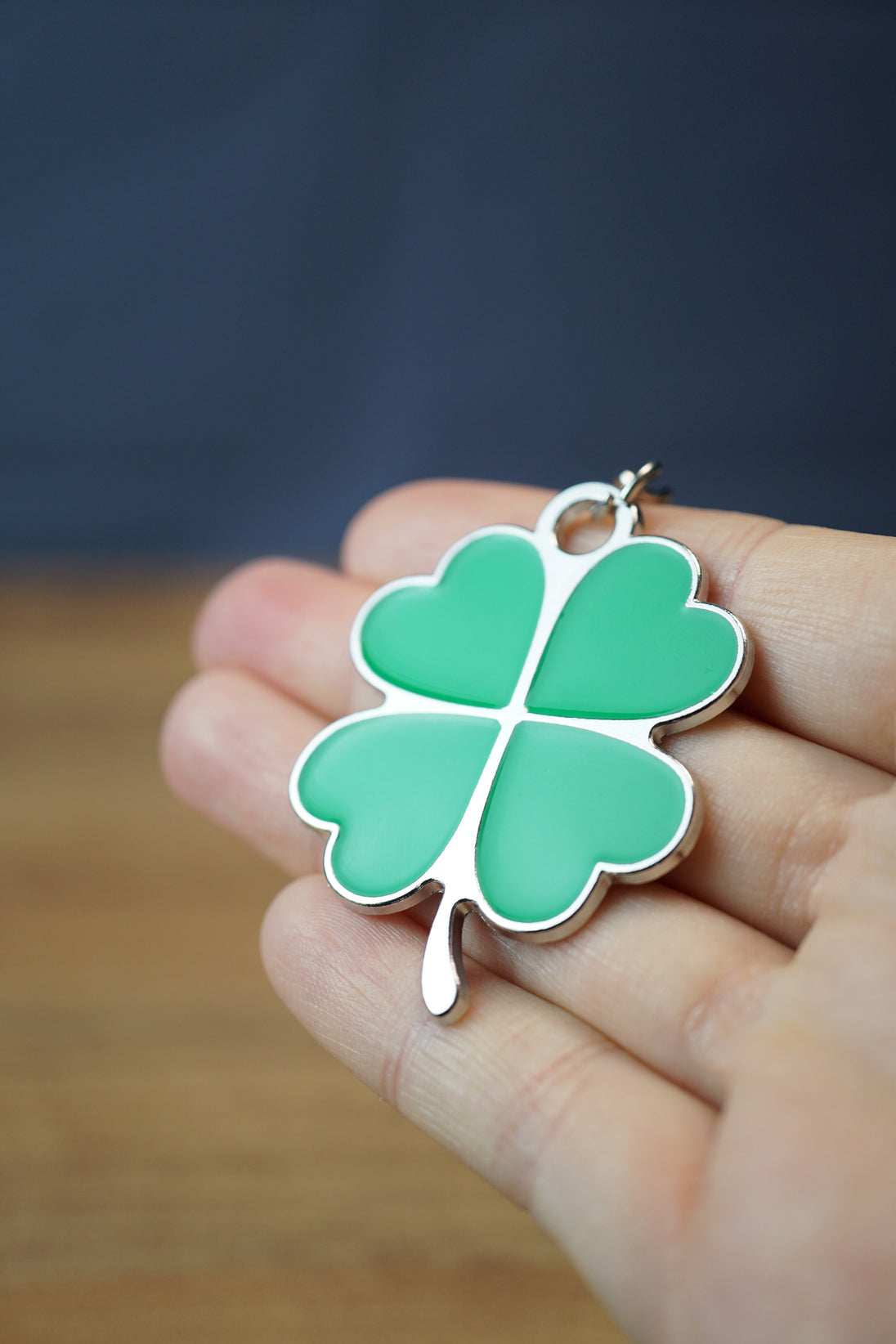 Green four leaf clover keychain charm held in hand, showing glossy clover leaves, silver metal border, and compact lucky accessory design.