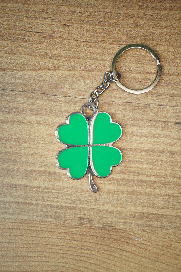 Green four leaf clover keychain with silver metal trim and chain, displayed flat on a wooden surface for a lucky charm accessory photo.