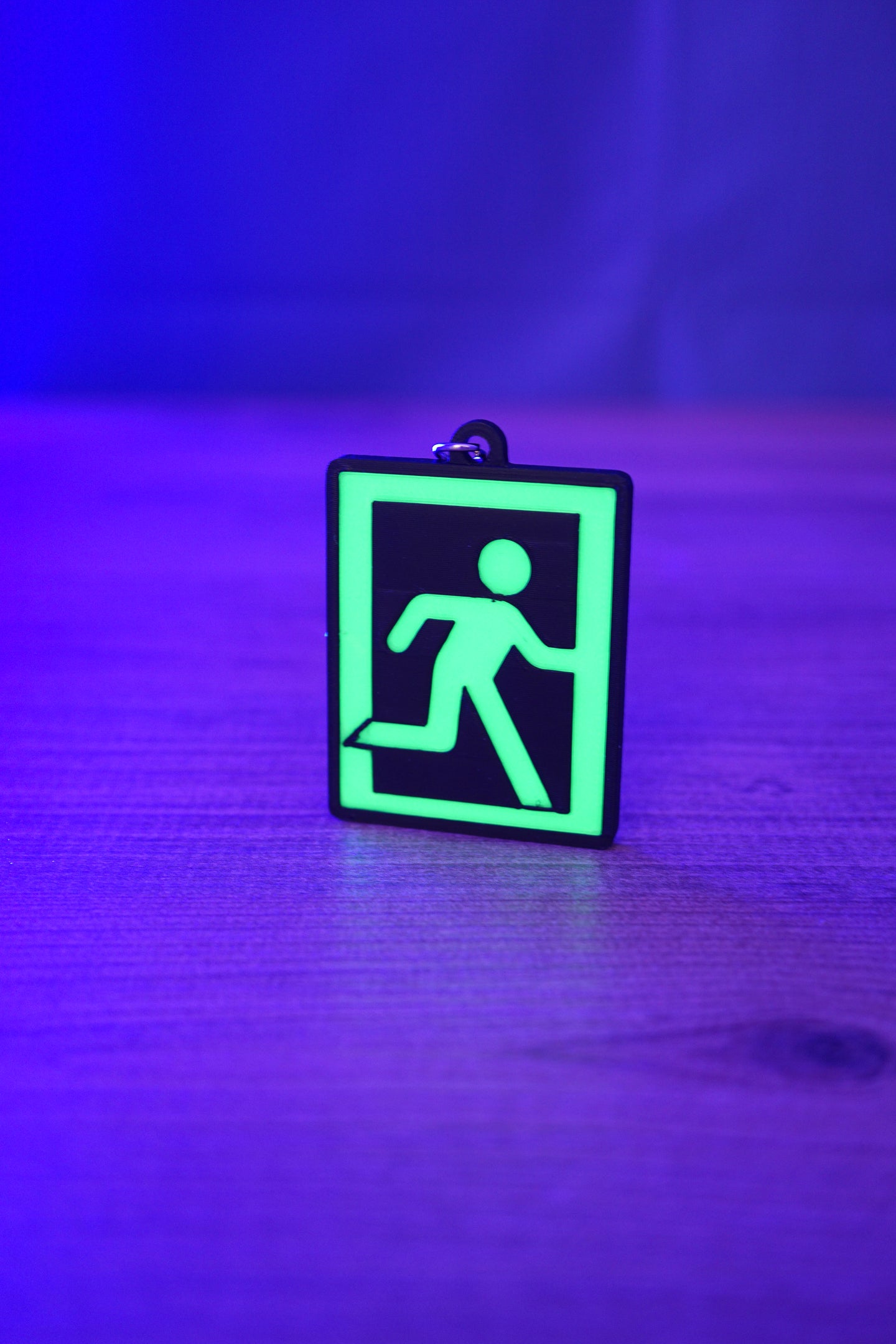 Glow-in-the-dark extraction keyring standing on a wooden table under blue and purple lighting, with the green running figure design brightly illuminated.
