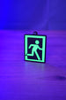 Glow-in-the-dark extraction keyring standing on a wooden table under blue and purple lighting, with the green running figure design brightly illuminated.
