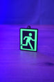 Glow-in-the-dark extraction keyring standing on a wooden table under blue and purple lighting, with the green running figure design brightly illuminated.