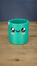 Green Palia-inspired Cyl pen pot shown empty from the front, featuring large black eyes, a smiling face, pink cheeks and decorative rim detail