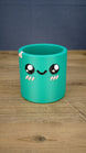 Green Palia-inspired Cyl pen pot shown empty from the front, featuring large black eyes, a smiling face, pink cheeks and decorative rim detail
