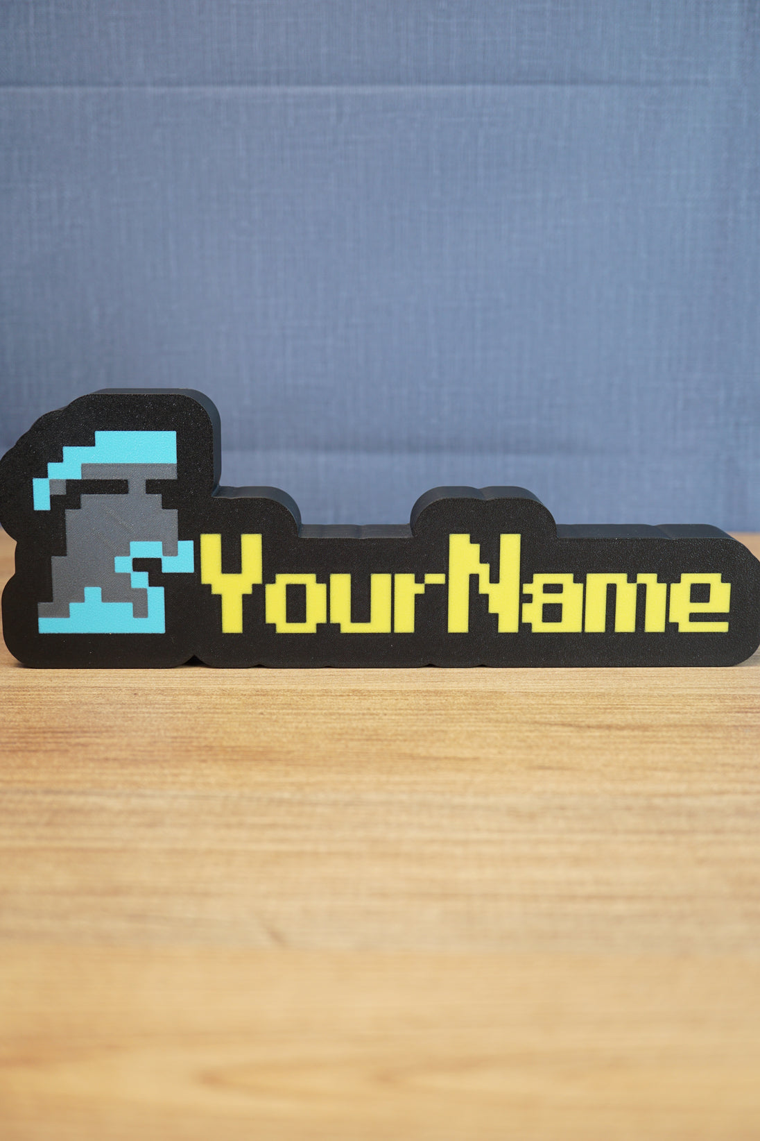 Custom RuneScape-style group ironman nameplate with a blue and grey helmet icon, yellow lettering, and black frame displayed on a wooden tabletop.