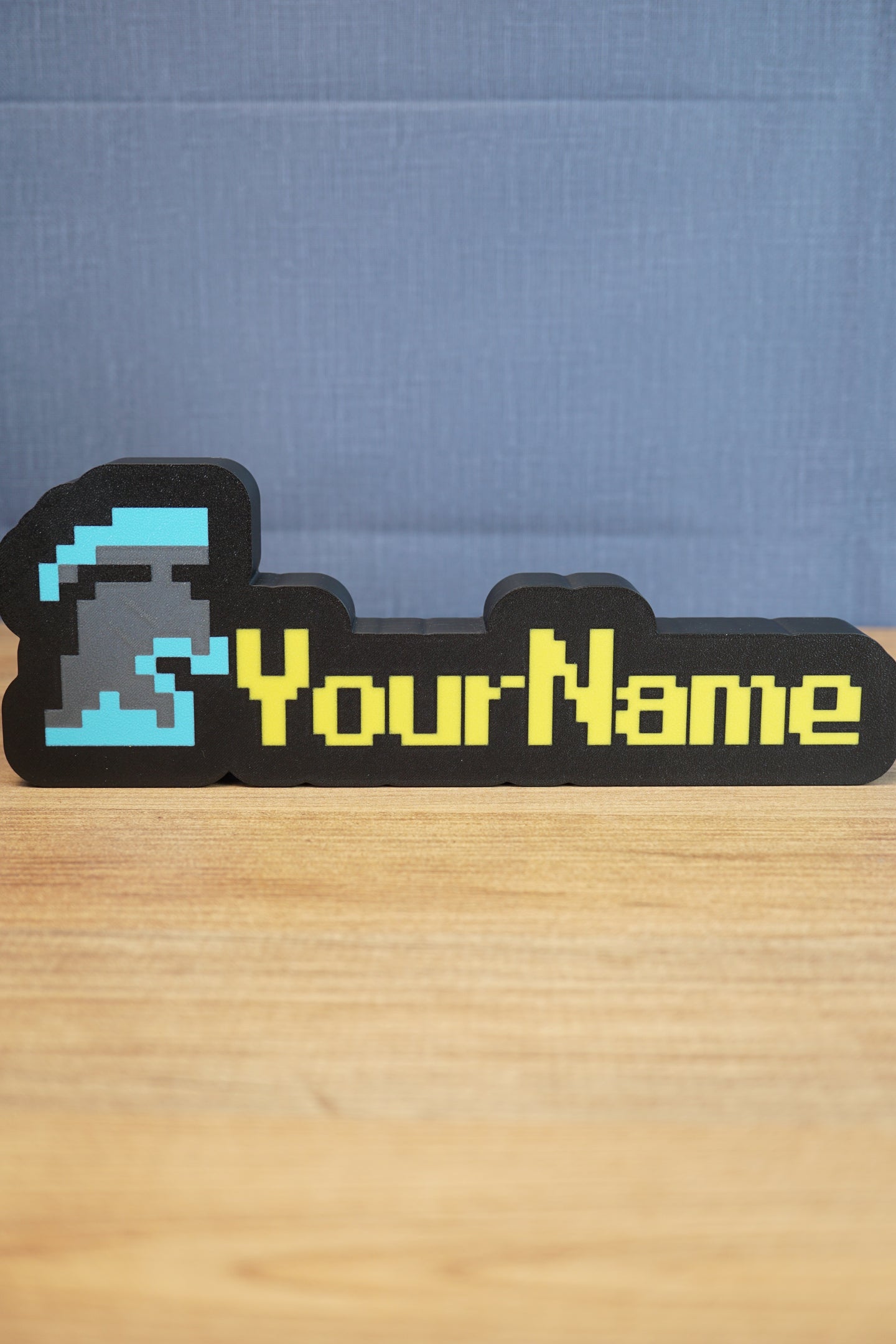 Custom RuneScape-style group ironman nameplate with a blue and grey helmet icon, yellow lettering, and black frame displayed on a wooden tabletop.