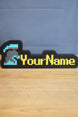 Custom RuneScape-style group ironman nameplate with a blue and grey helmet icon, yellow lettering, and black frame displayed on a wooden tabletop.