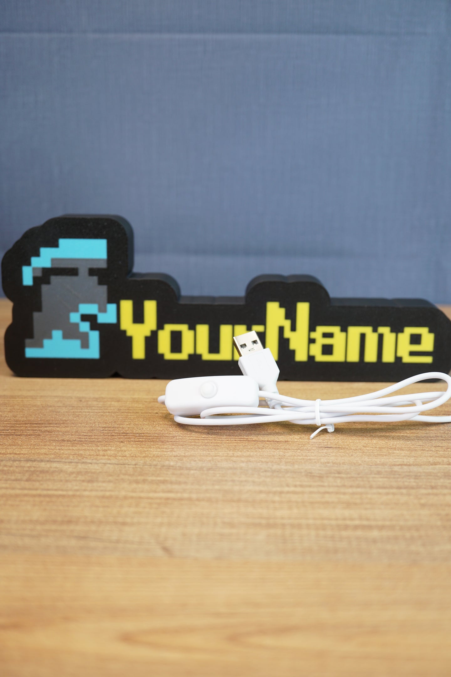 RuneScape-inspired group ironman nameplate with custom yellow lettering and blue helmet icon shown with USB cable accessory on a wooden desk.