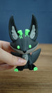 Hand holding a Cave Kitsuu 3D printed figure, highlighting its dark green body, bright green eyes, tall ears, and black paws.