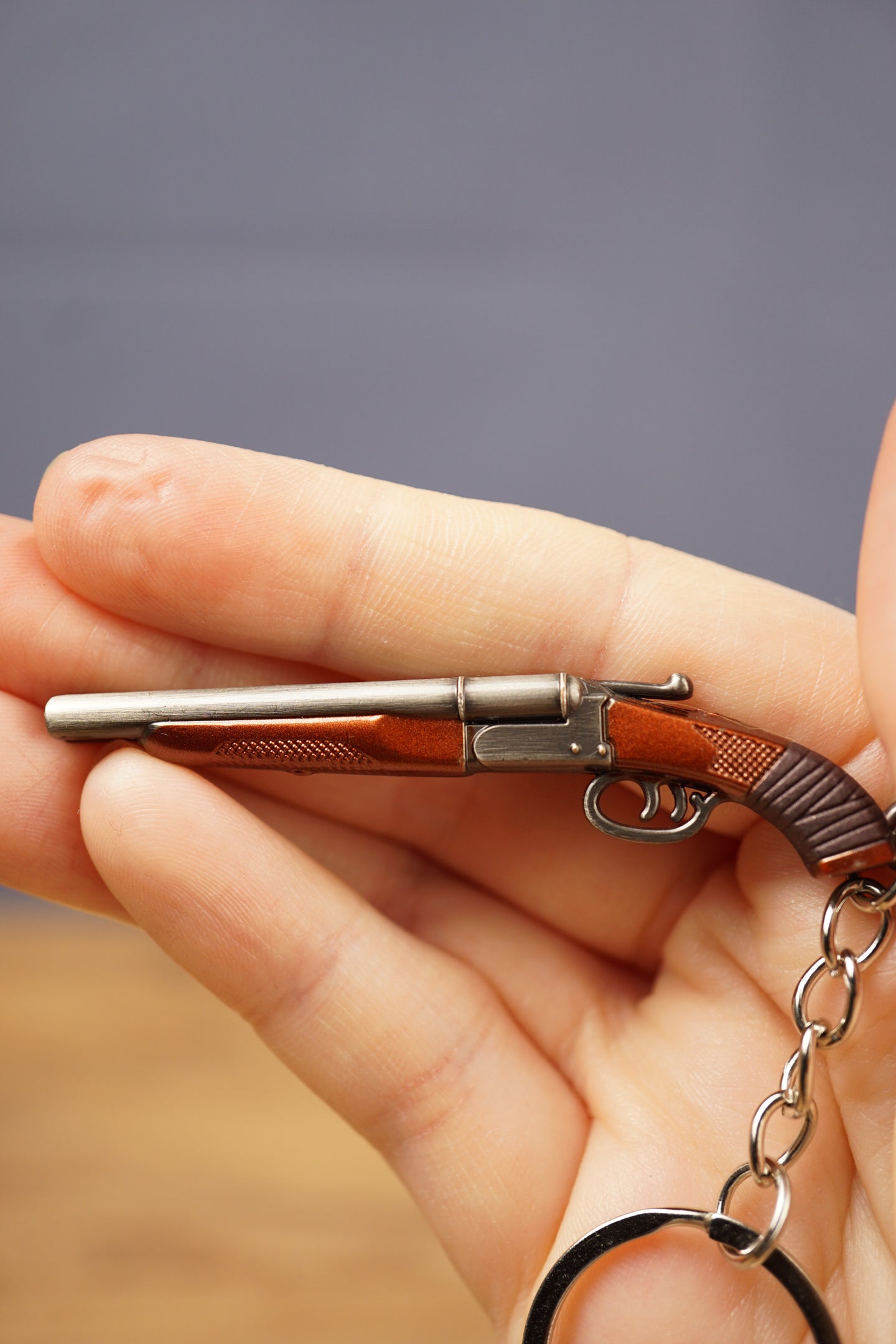 Hand holding a compact 12GA double-barrel shotgun keychain with metal finish, detailed grip texture and attached keyring chain