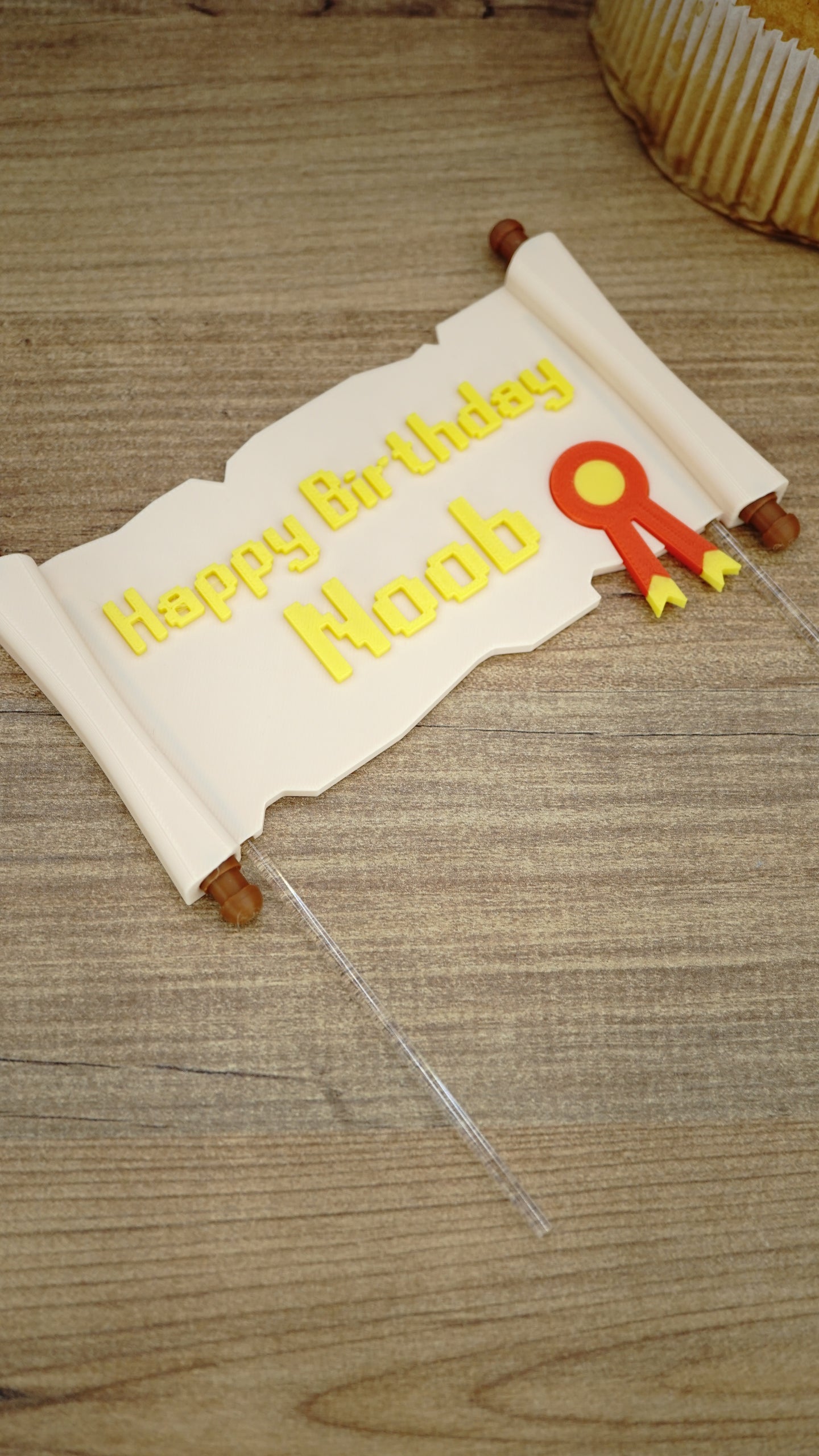 Custom Happy Birthday Noob quest scroll cake topper laid flat on a wooden surface with badge detail and clear acrylic cake sticks attached.