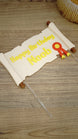 Custom Happy Birthday Noob quest scroll cake topper laid flat on a wooden surface with badge detail and clear acrylic cake sticks attached.