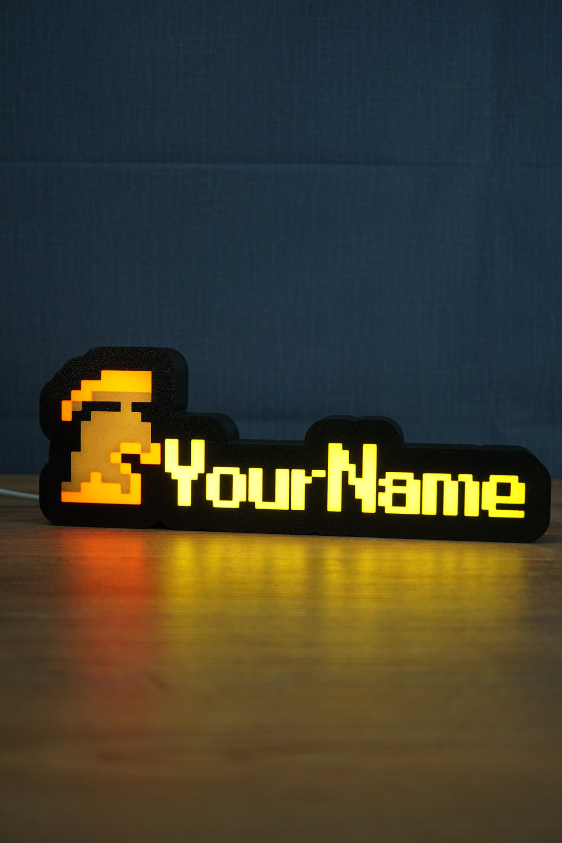 Glowing hardcore group ironman desk sign with red and grey helmet icon, yellow custom lettering, and warm reflection across the tabletop.