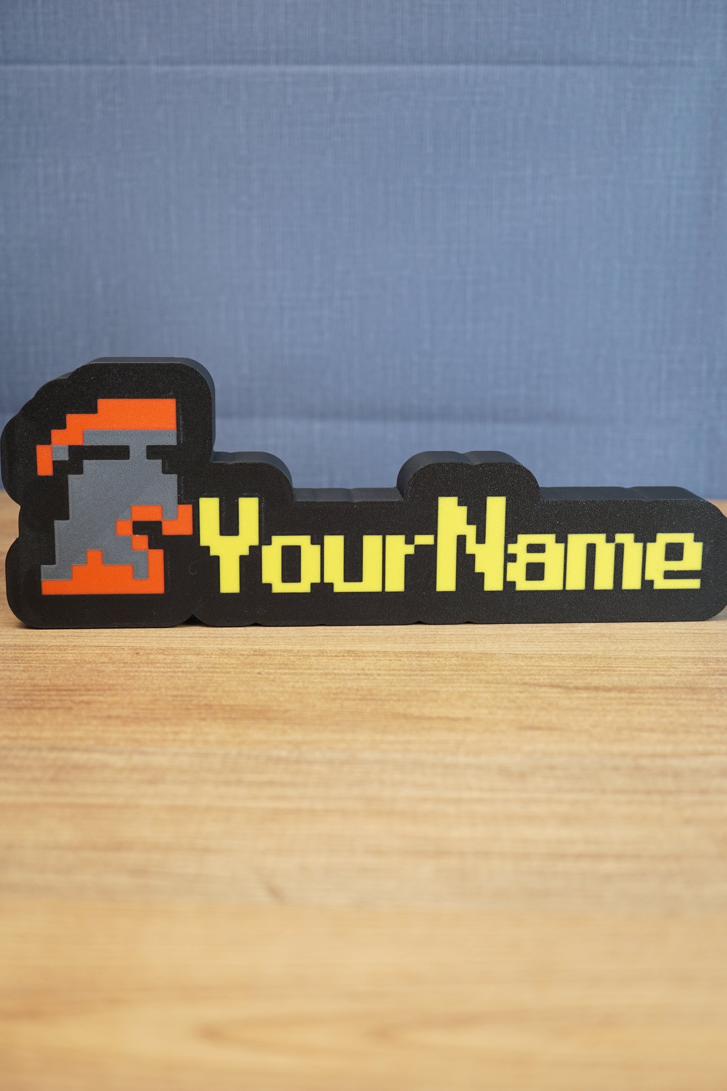 Custom hardcore group ironman nameplate with a red and grey helmet icon, yellow RuneScape-style lettering, and black border on a tabletop.