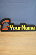 Custom hardcore group ironman nameplate with a red and grey helmet icon, yellow RuneScape-style lettering, and black border on a tabletop.