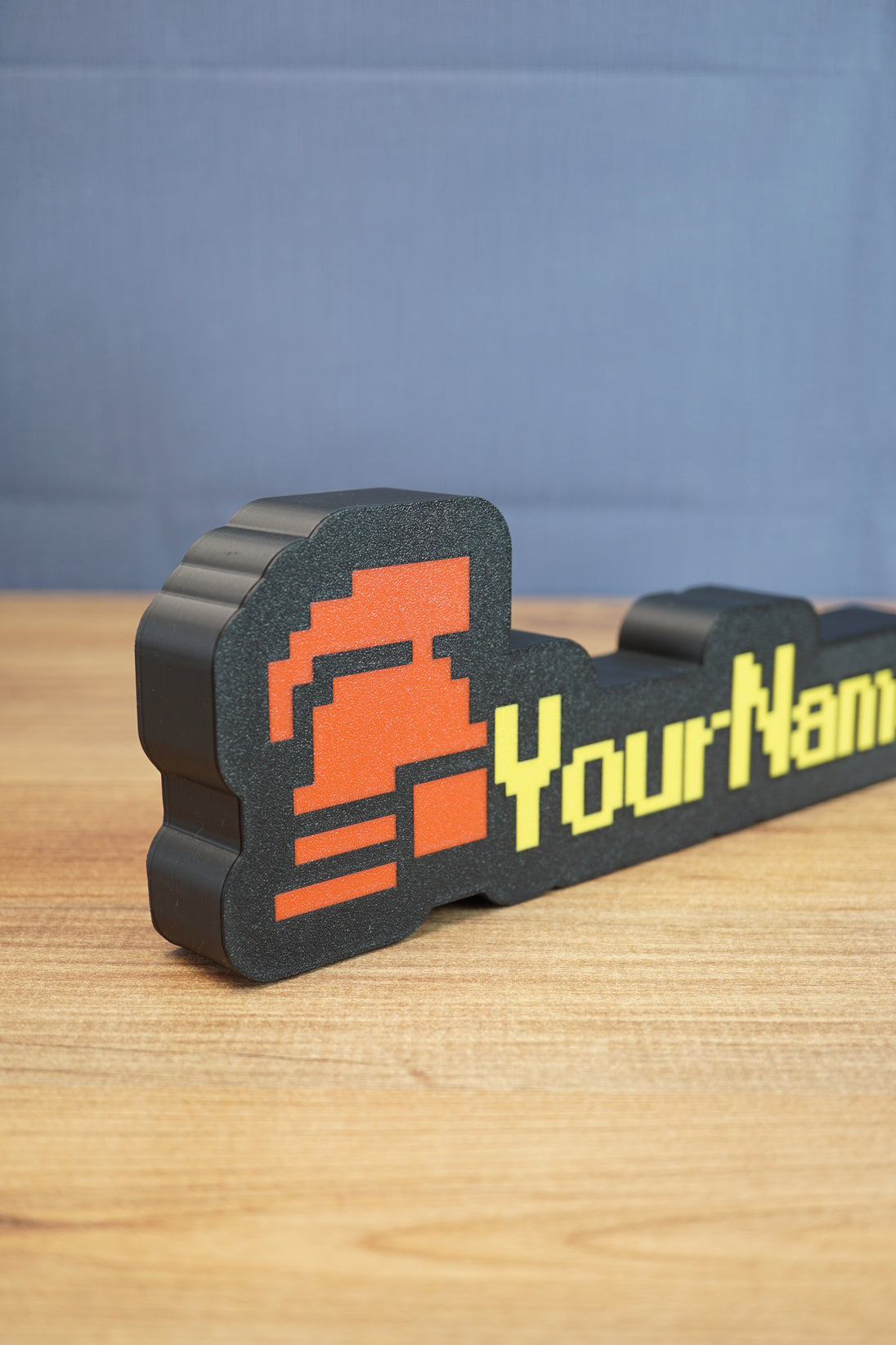 Angled view of a hardcore ironman desk nameplate featuring a red helmet icon, yellow RuneScape-style text, and black outer frame.