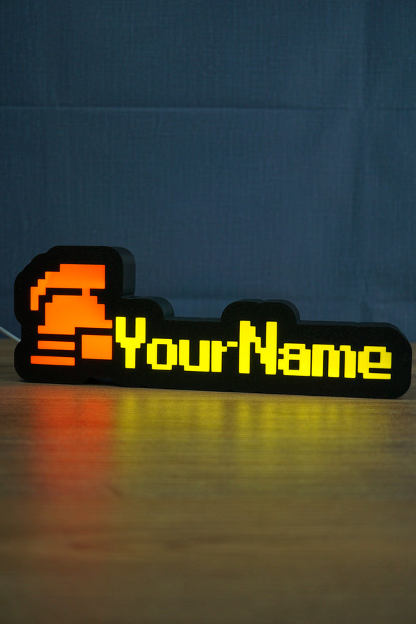 Glowing hardcore ironman desk sign with a red helmet icon, bright yellow personalized text, and warm reflection across the desk surface.