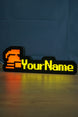 Glowing hardcore ironman desk sign with a red helmet icon, bright yellow personalized text, and warm reflection across the desk surface.
