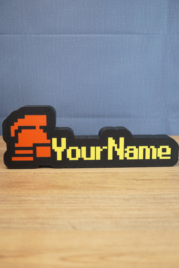 Custom hardcore ironman RuneScape-style nameplate with a red helmet icon, bold yellow lettering, and black casing on a tabletop.
