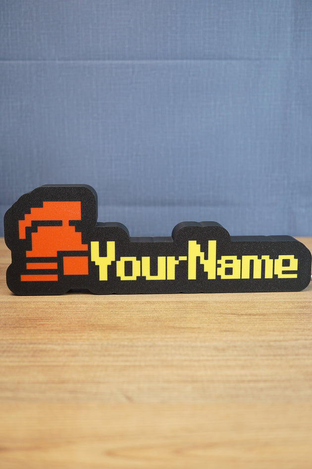 Custom hardcore ironman RuneScape-style nameplate with a red helmet icon, bold yellow lettering, and black casing on a tabletop.