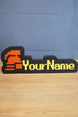 Custom hardcore ironman RuneScape-style nameplate with a red helmet icon, bold yellow lettering, and black casing on a tabletop.