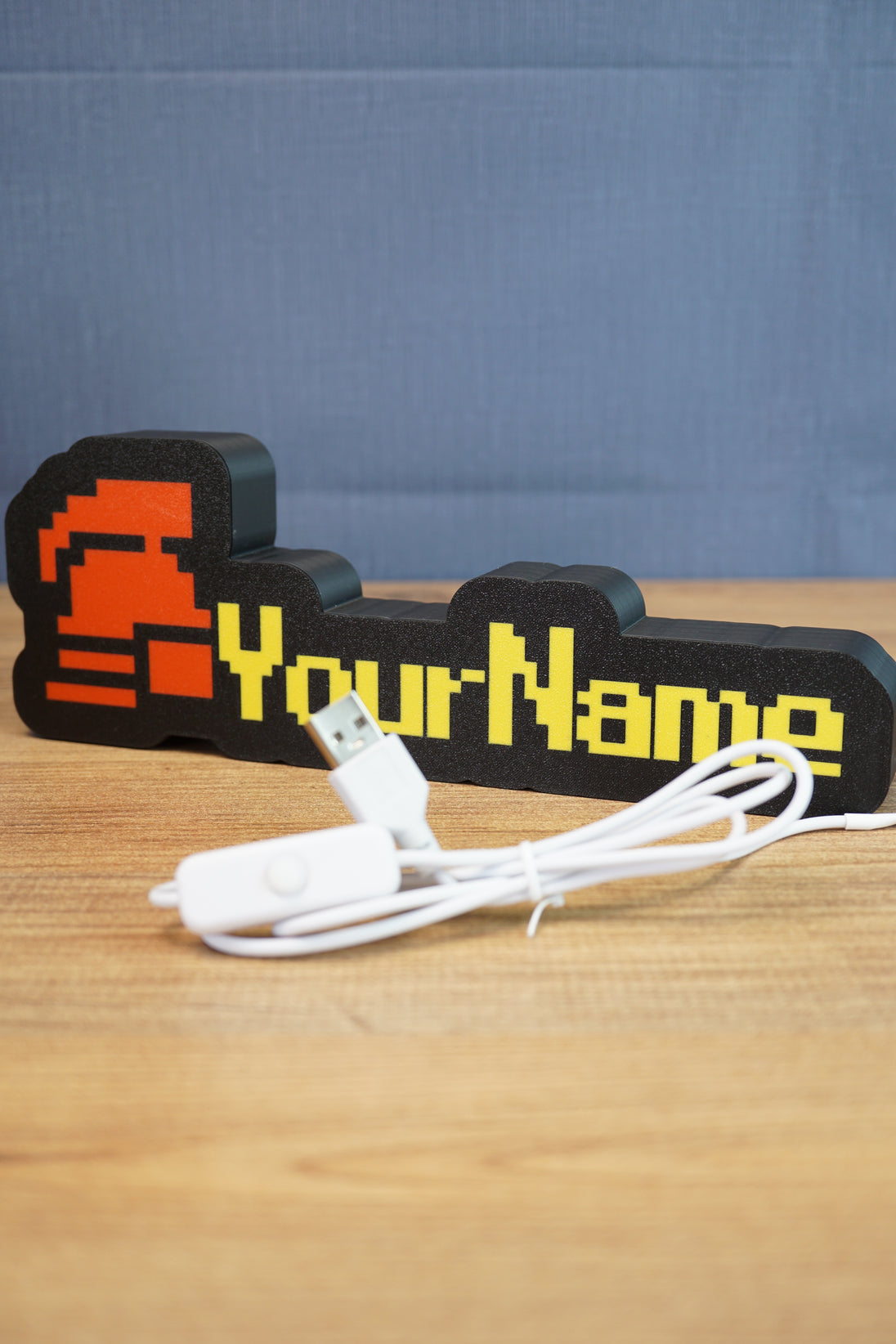 Hardcore ironman RuneScape-inspired nameplate shown with USB cable, red helmet icon, yellow lettering, and black casing on a wooden surface
