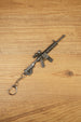 Angled HK 416A5 rifle keychain replica on wooden surface with detailed stock, magazine, optic, rail system and keyring chain