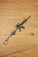 Angled HK 416A5 rifle keychain replica on wooden surface with detailed stock, magazine, optic, rail system and keyring chain