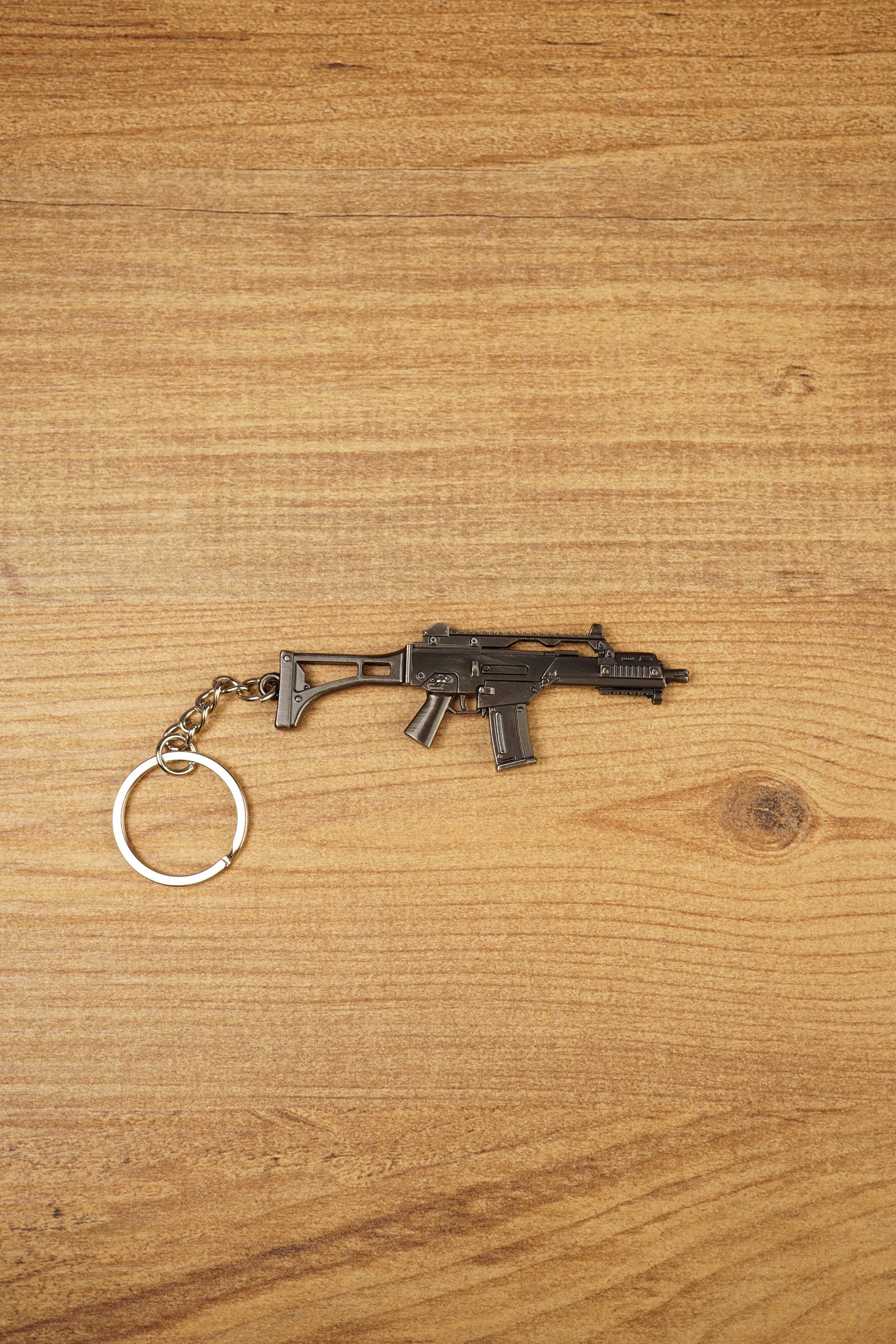 HK G36 metal rifle keyring laid flat on a wood surface, detailed tactical FPS gamer keychain with silver ring and chain