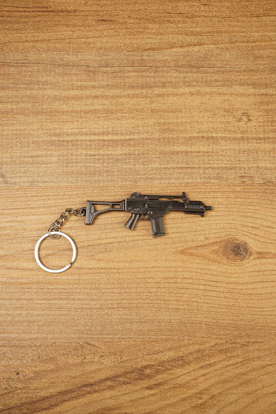 HK G36 metal rifle keyring laid flat on a wood surface, detailed tactical FPS gamer keychain with silver ring and chain