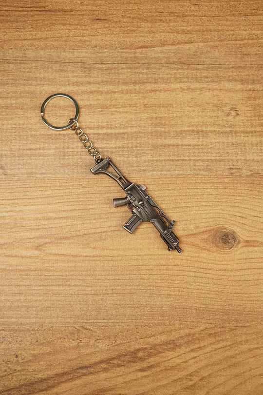 HK G36 rifle keyring angled on a wooden tabletop, compact metal gamer keychain for tactical shooter and FPS fans