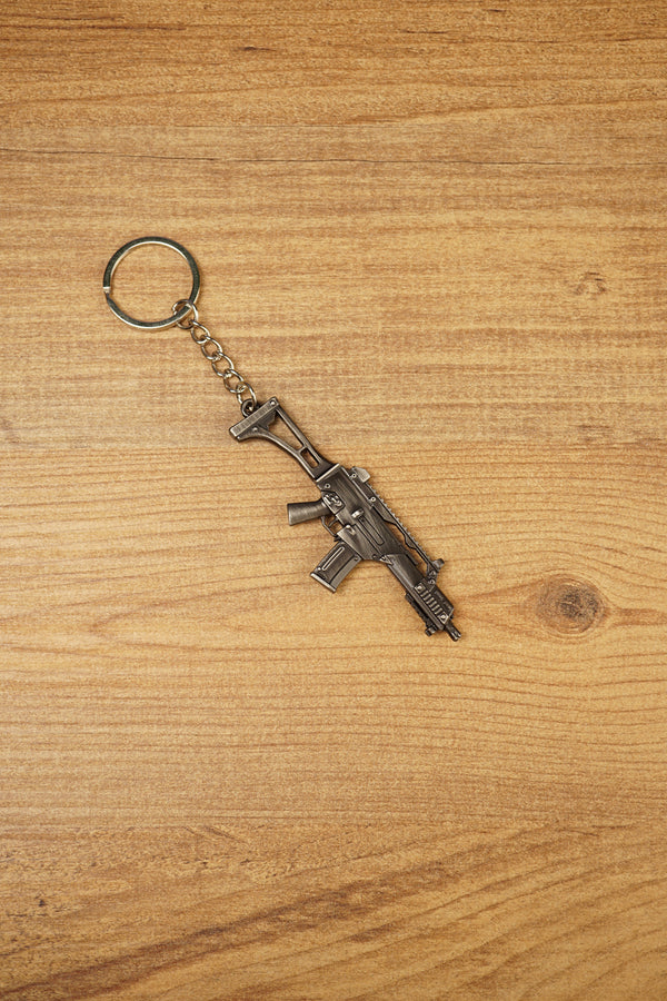 HK G36 rifle keyring angled on a wooden tabletop, compact metal gamer keychain for tactical shooter and FPS fans
