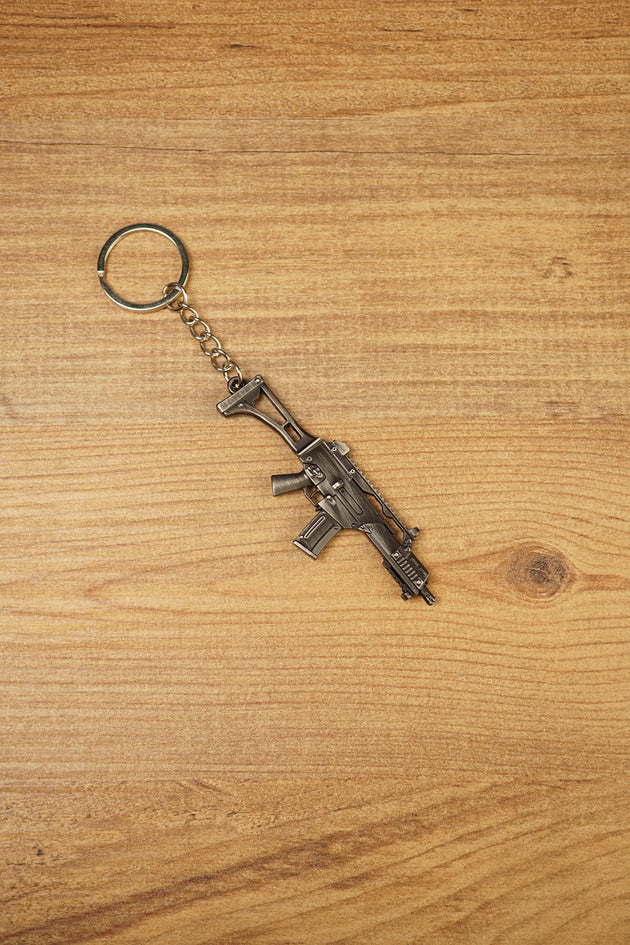 HK G36 rifle keyring angled on a wooden tabletop, compact metal gamer keychain for tactical shooter and FPS fans