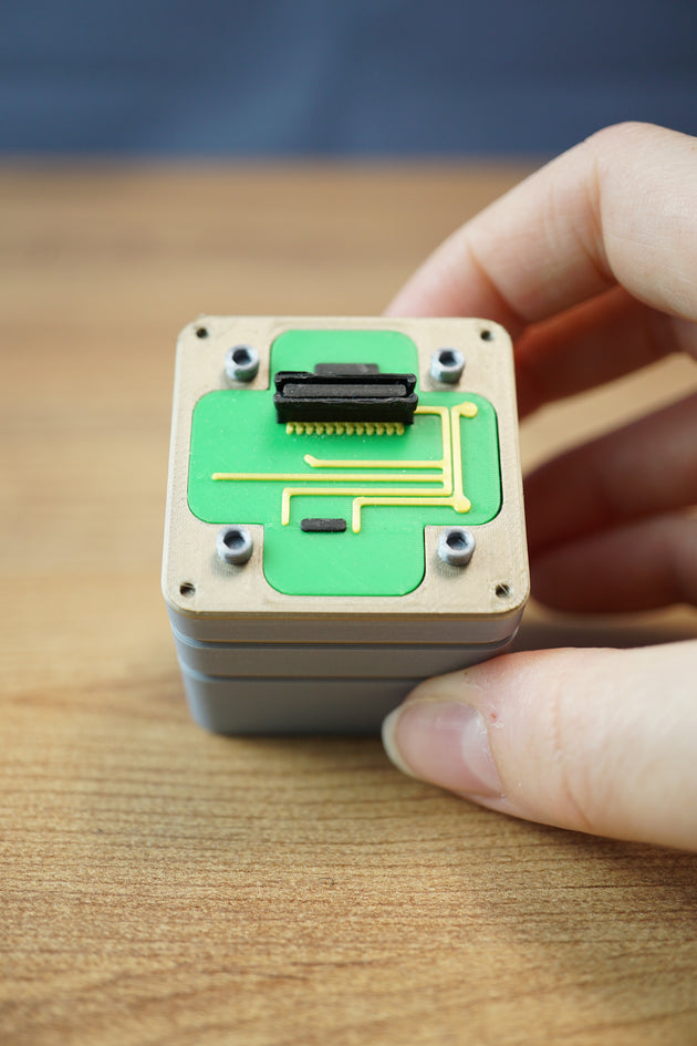 Close-up of an Iridium thermal vision module replica held in hand, featuring green circuit styling, grey casing, and detailed top connector.