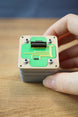 Close-up of an Iridium thermal vision module replica held in hand, featuring green circuit styling, grey casing, and detailed top connector.